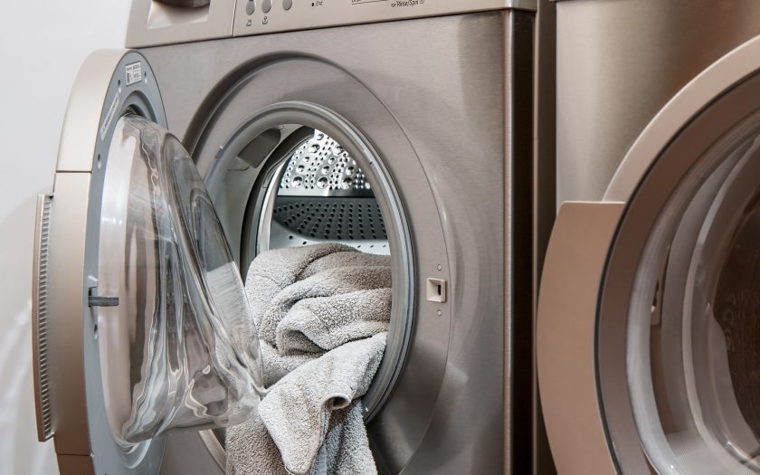 Aus einer Waschmaschinen Türe hängt Wäsche raus.